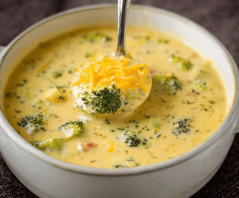 A bowl of creamy potato broccoli cheddar soup garnished with shredded cheese and fresh herbs, served with crusty bread on a rustic wooden table.