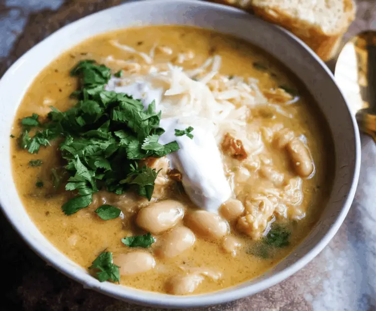 Creamy White Bean Enchilada Soup in a bowl topped with cheese, cilantro, and sour cream, served with tortilla chips on a rustic wooden table