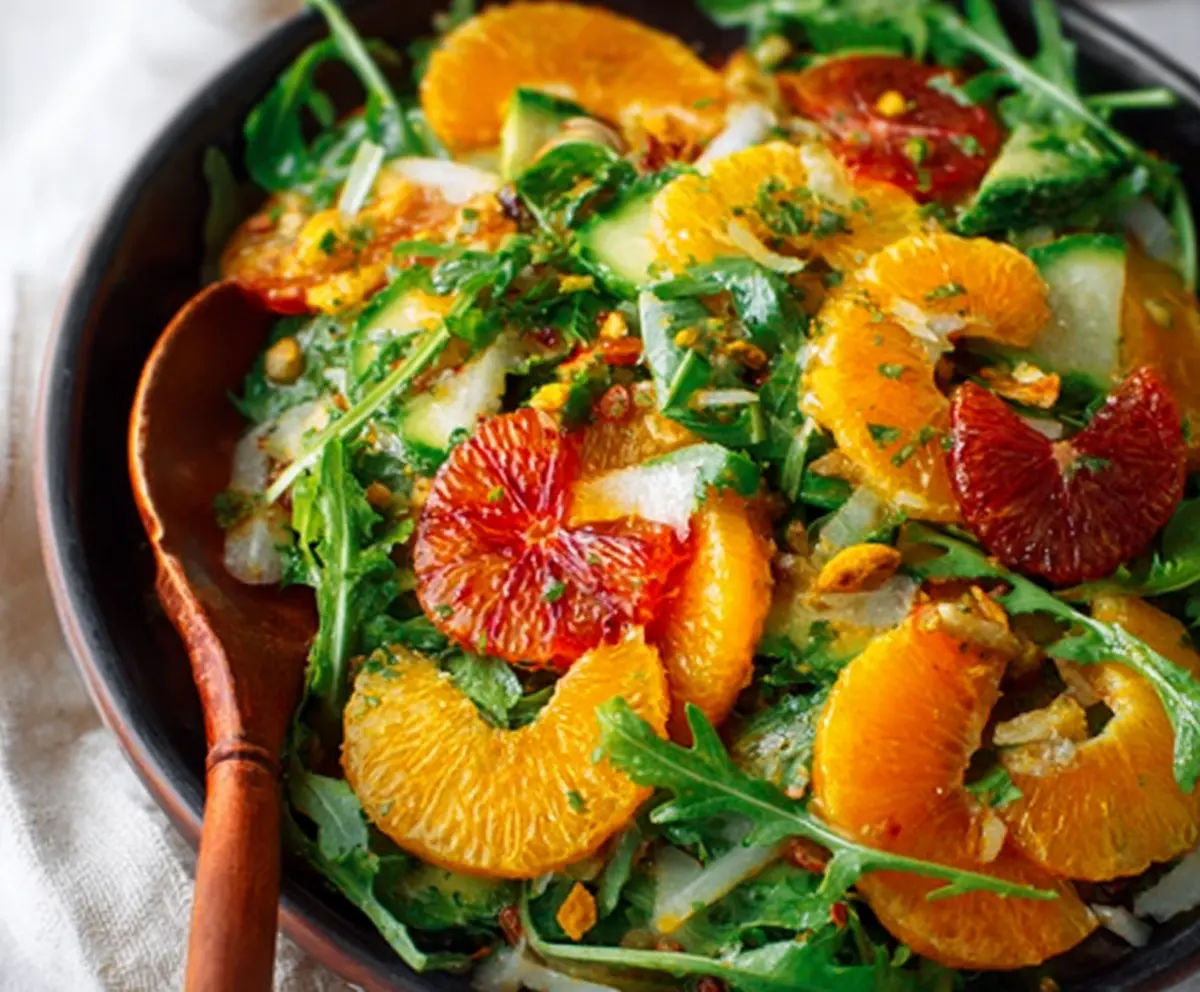 Fresh winter citrus and peppery arugula salad garnished with herbs on a white plate.