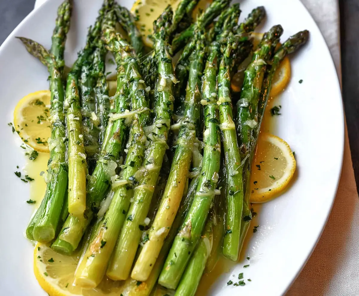 Fresh lemon butter glazed asparagus spears on a white plate, ready for a healthy side dish.
