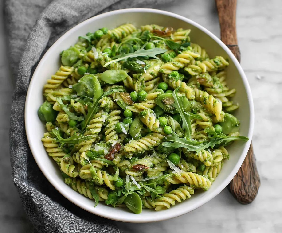 Delicious spring pea pesto pasta garnished with fresh herbs on a white plate.